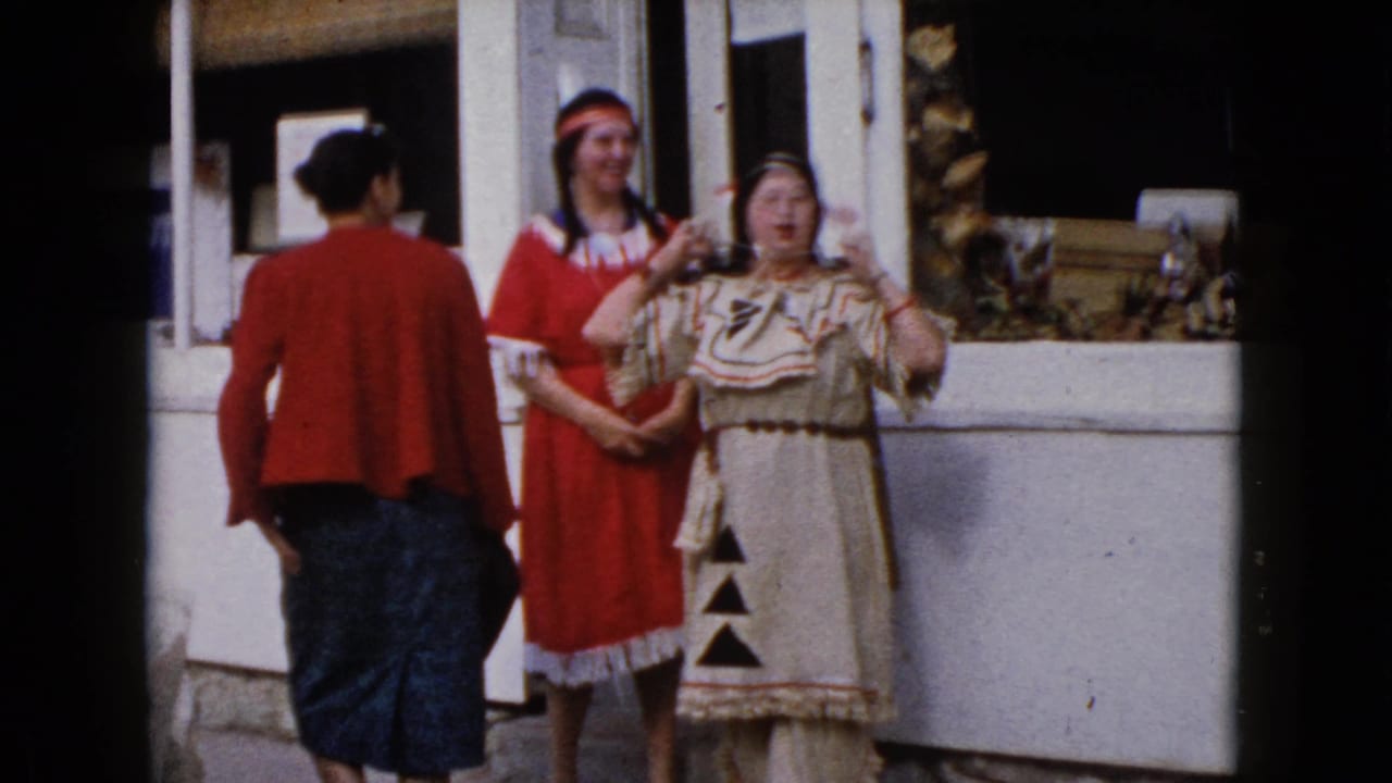 Adult women outside a Wauconda storefront in 1960, with two wearing Native American-inspired costumes and headwear.