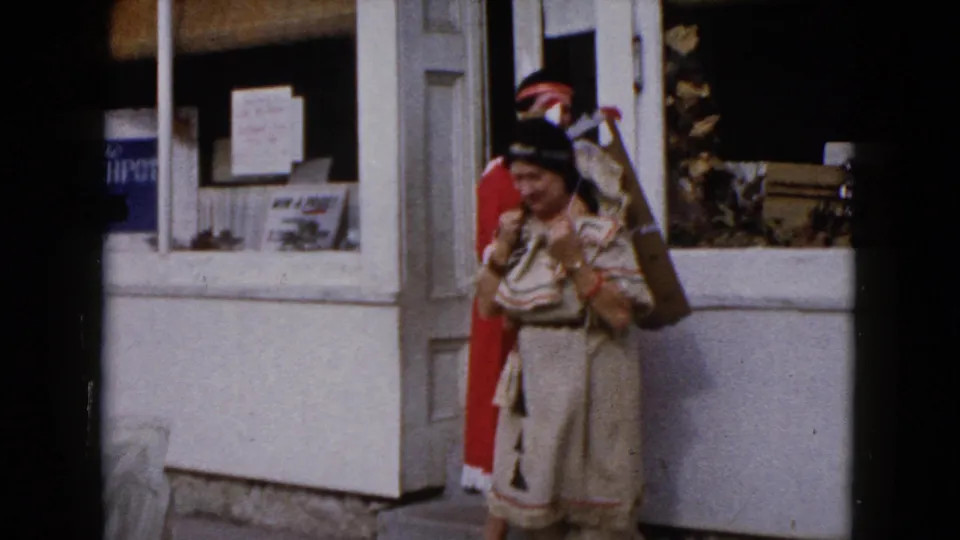 End frame from 1960 Wauconda footage showing a woman in Native American-inspired costume beside a storefront.