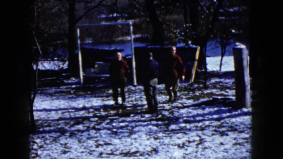 1960 Wauconda winter frame showing three people walking through a snowy yard near the same white swing frame and trees.