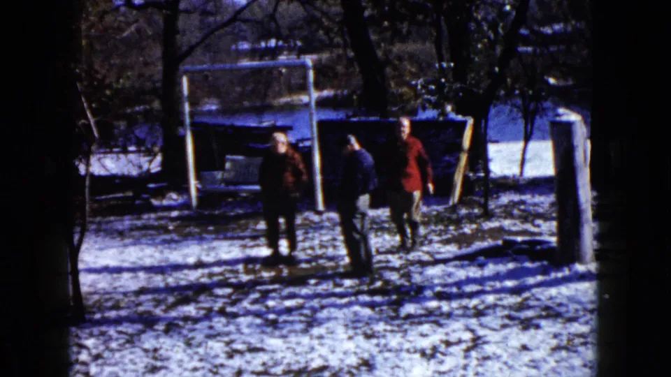 1960 Wauconda winter yard view with three people near the swing frame, snow on the ground, trees, and water behind them.