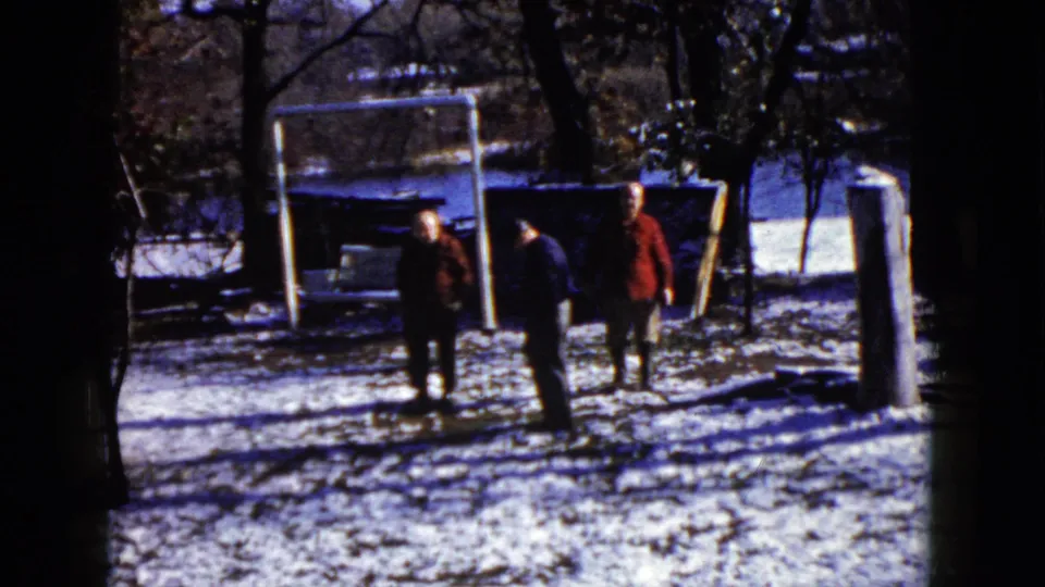 Final 1960 Wauconda frame shows two adults near center and a third at right, all in a snowy yard with bare trees and a white goal frame behind them.