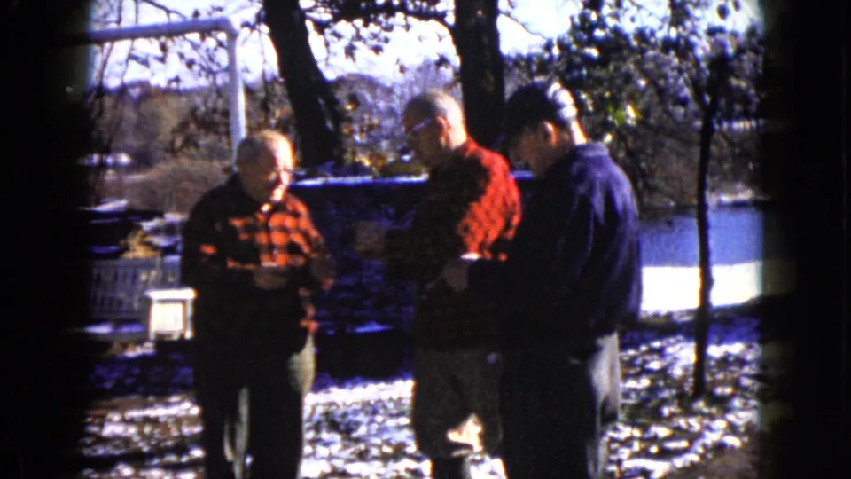 At the end of the clip, three older men remain gathered in a snowy Wauconda setting, looking down at papers near trees and water.