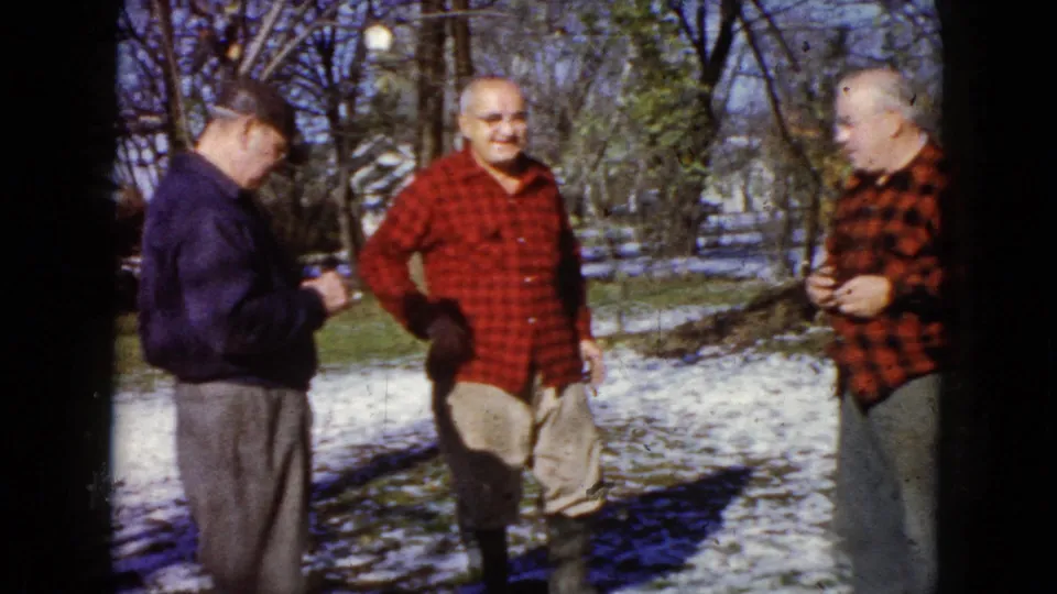 Three older men gather in a snow-dusted yard in 1960 Wauconda, including two in red plaid shirts and one in a dark jacket.