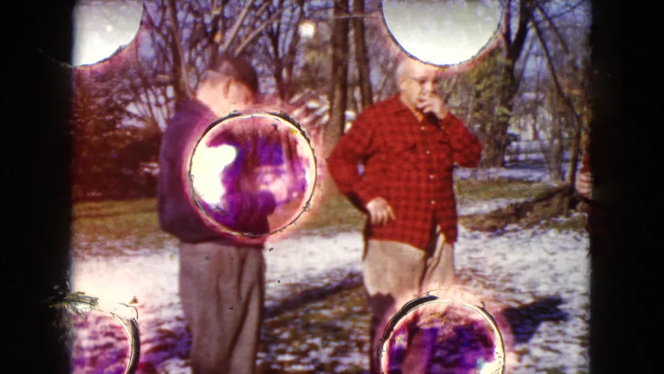 Three older men remain in the snowy Wauconda yard while bright 8mm light flare and gate marks obscure part of the 1960 frame.