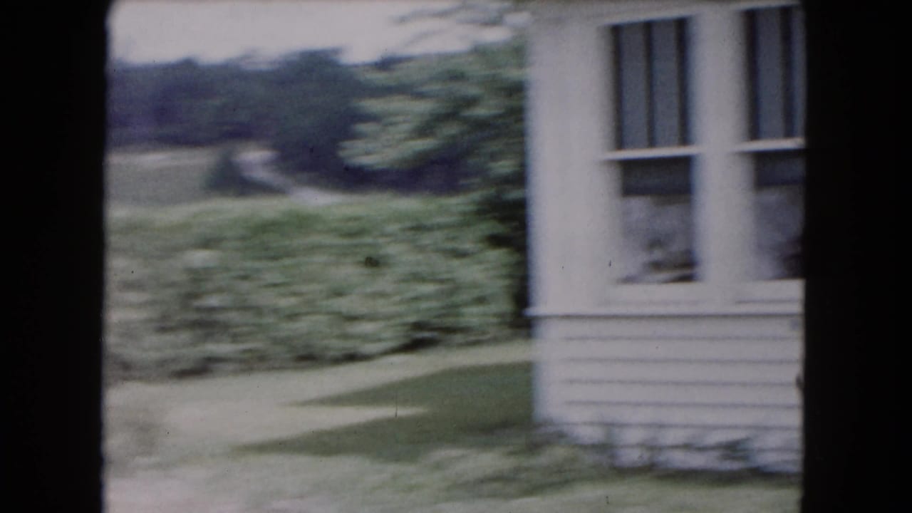 Blurred view of a house edge, lawn, shrubs, and a path as the camera shifts.