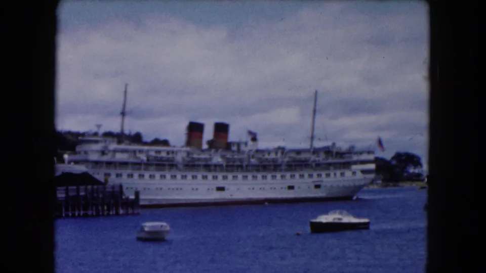 A side-on harbor view shows the white passenger ship docked near wooden pier pilings, with small motorboats drifting in front.