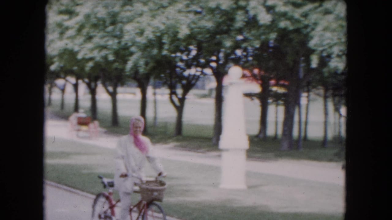 Smiling woman with a bicycle pauses or rides near a white park monument.