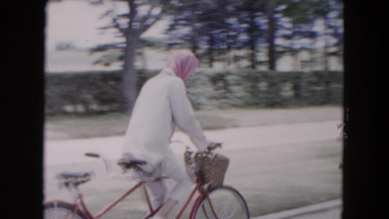 Bandanna-wearing cyclist rides a red tandem bicycle along a tree-lined road.