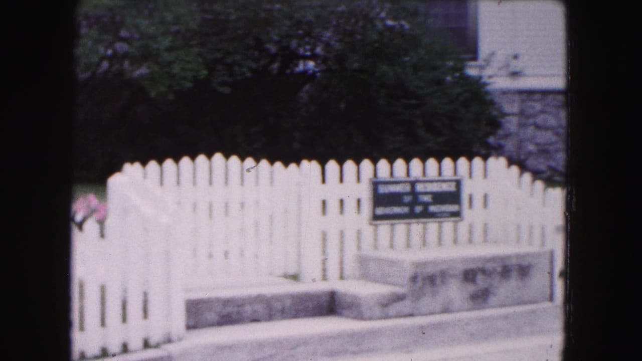 White picket fence with a posted sign in front of a landscaped residence.