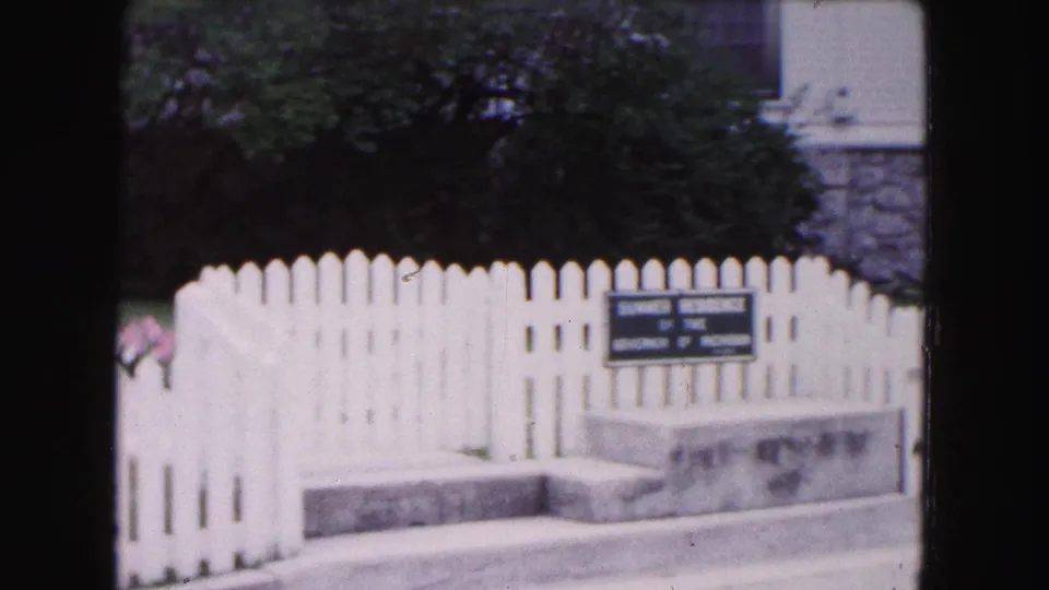 1961 Buffalo-area 8mm frame showing a white picket fence, stone curb, flower bed, and posted residence sign near a house entrance.