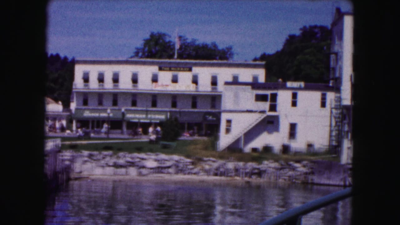 1961 Buffalo waterfront view from a bridge, showing low white buildings, water, shoreline rocks, and trees in soft 8mm color.