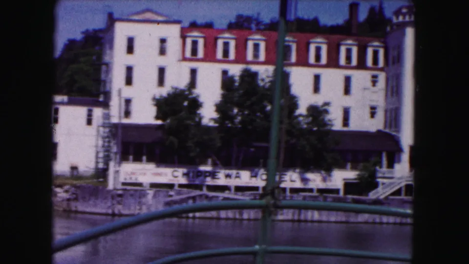 1961 Buffalo waterfront hotel view, with a tall white facade, red roof details, trees, awnings, river, and bridge railings in the foreground.
