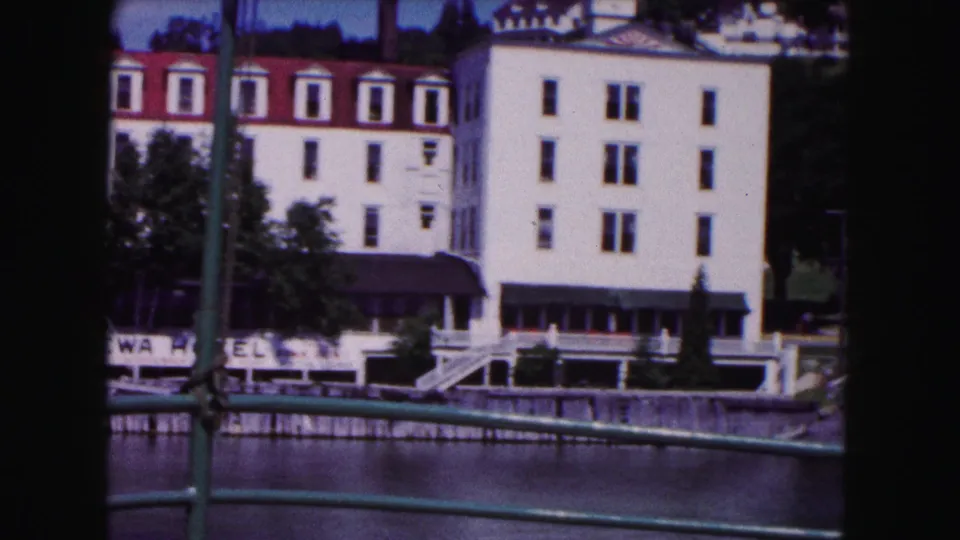 1961 Buffalo riverfront hotel and shoreline viewed from a bridge, with railings crossing the frame and a partial hotel sign below.