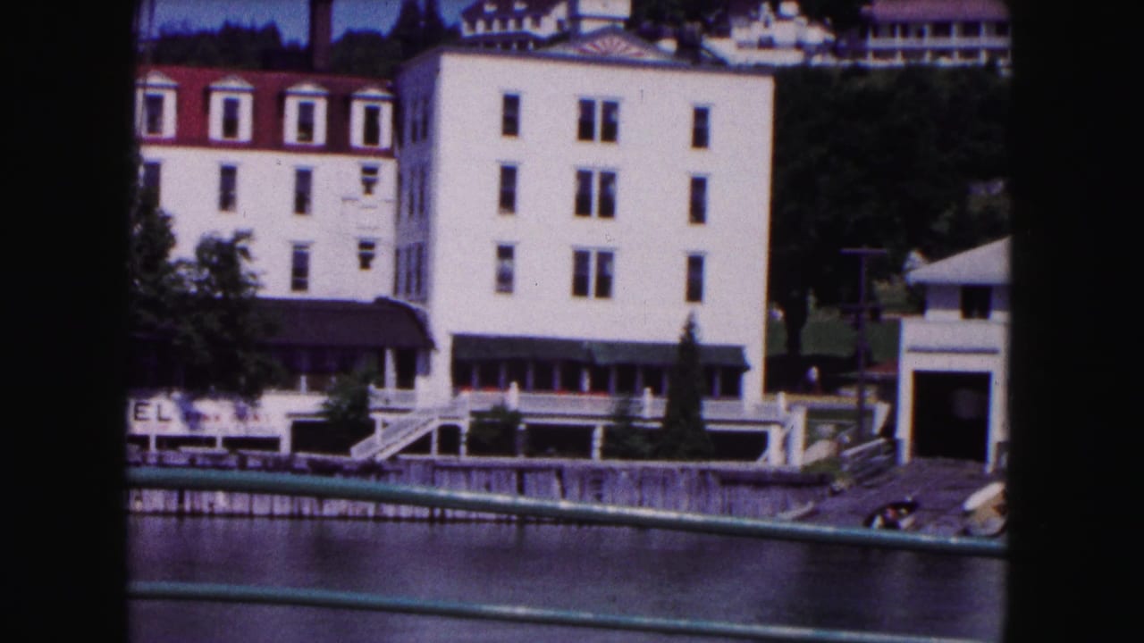 1961 Buffalo home-movie frame showing white riverside buildings with red roofs, a dock edge, trees, and a green railing in the foreground.