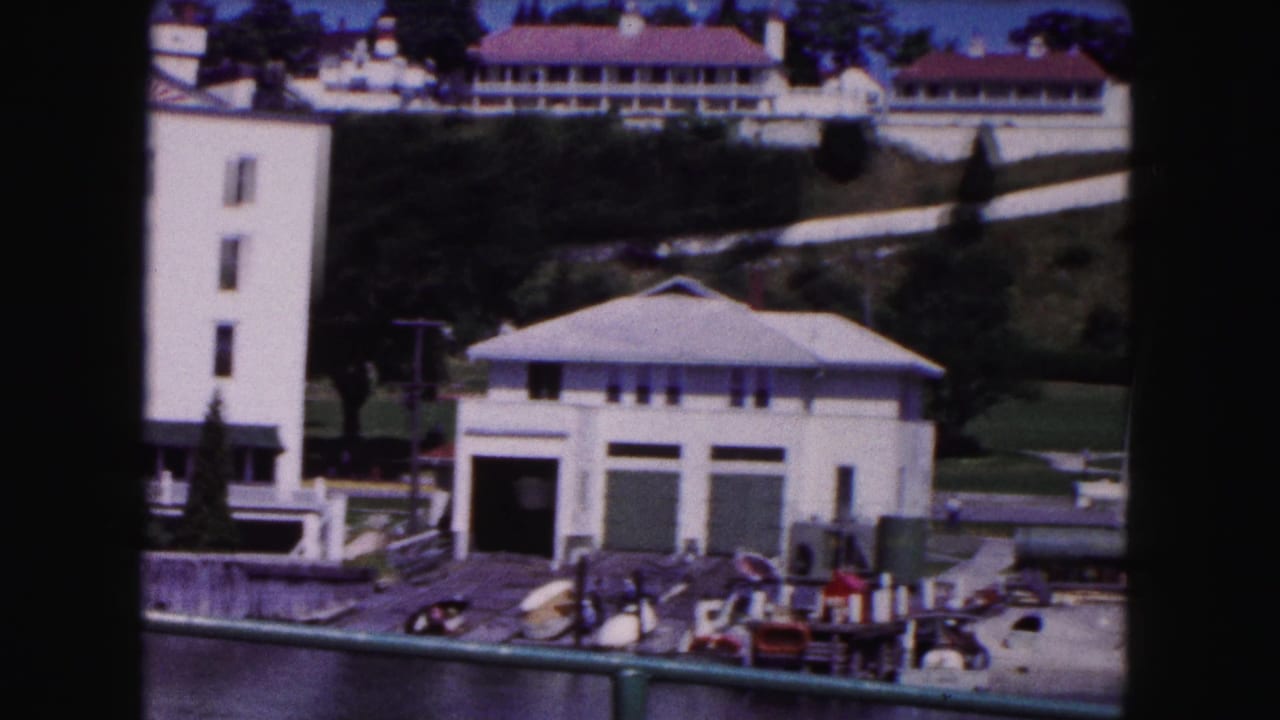 Boathouse-like building, dock equipment, hillside path, and red-roofed buildings above.