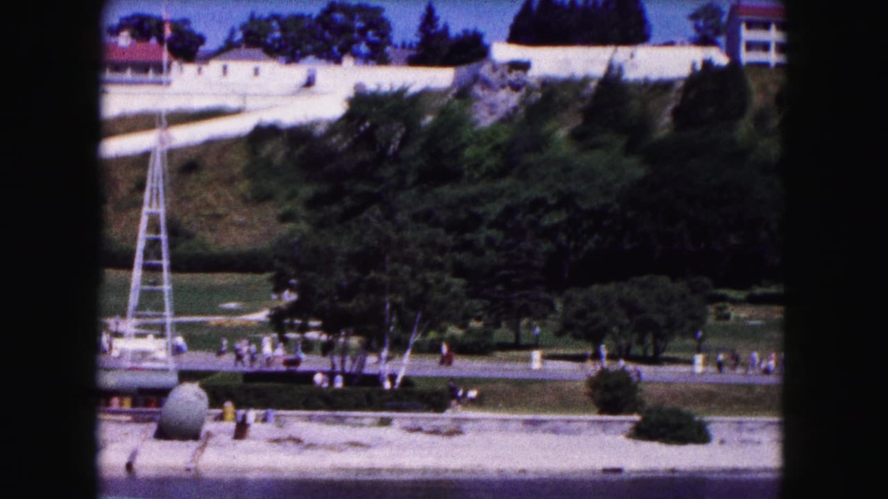 1961 Buffalo 8mm view of a hillside complex with white buildings, red roofs, a lattice tower, greenery, and distant pedestrians.