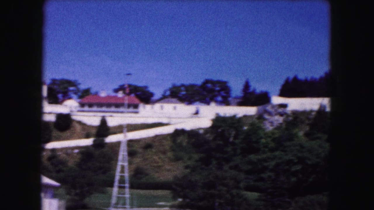 White hillside buildings with red roofs above trees and a pale lattice tower.