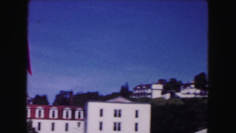 1961 Buffalo 8mm frame with a white red-roofed building in front and more hillside buildings among trees in the distance.