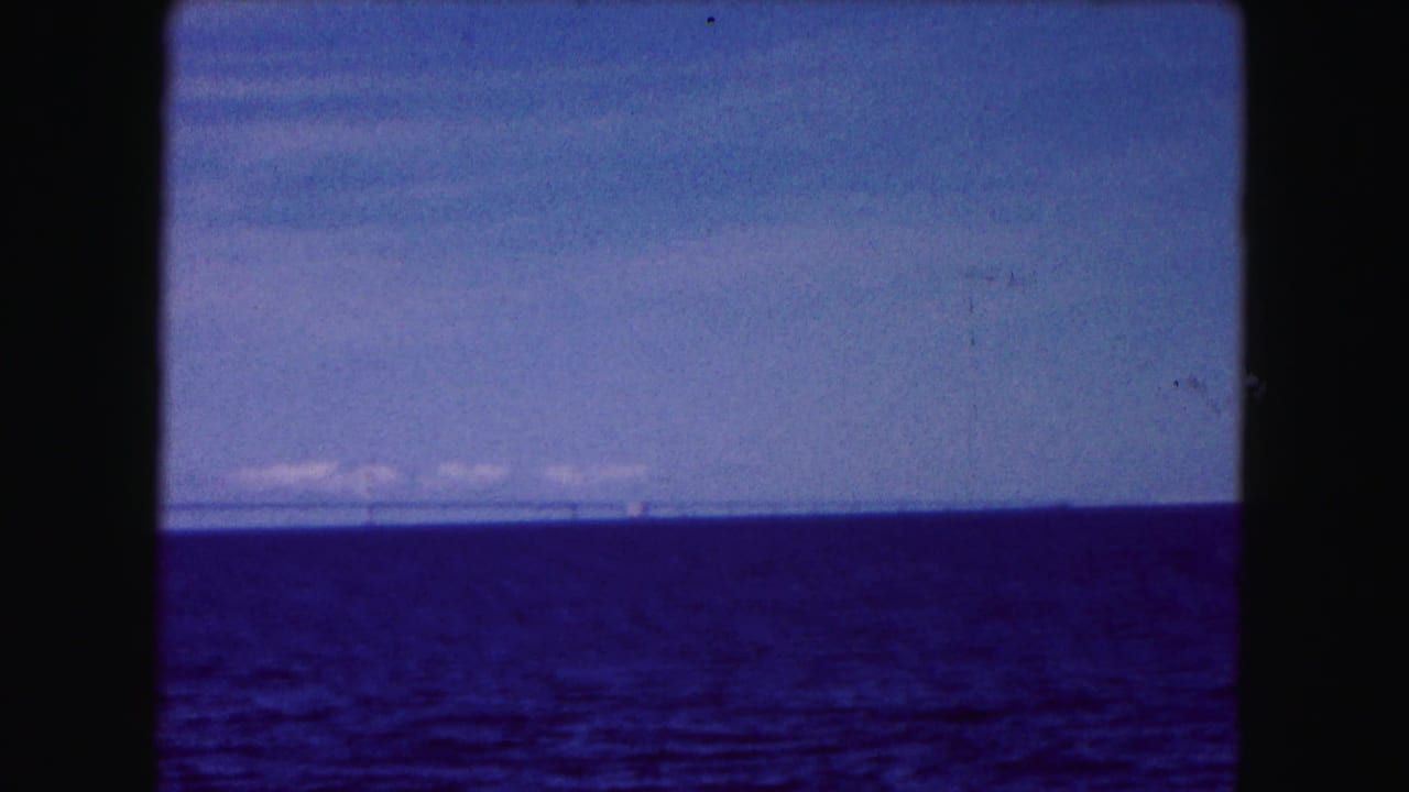 1961 Buffalo, New York 8mm frame showing open blue water, pale sky, thin clouds, and a distant bridge near the horizon.