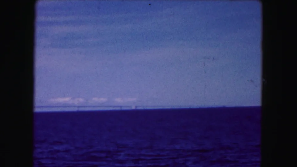 1961 Buffalo, New York 8mm frame showing open blue water, pale sky, thin clouds, and a distant bridge near the horizon.