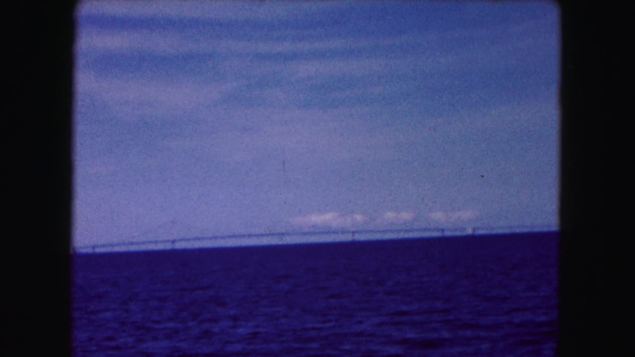 Distant bridge spans the horizon above dark blue water beneath a pale sky.