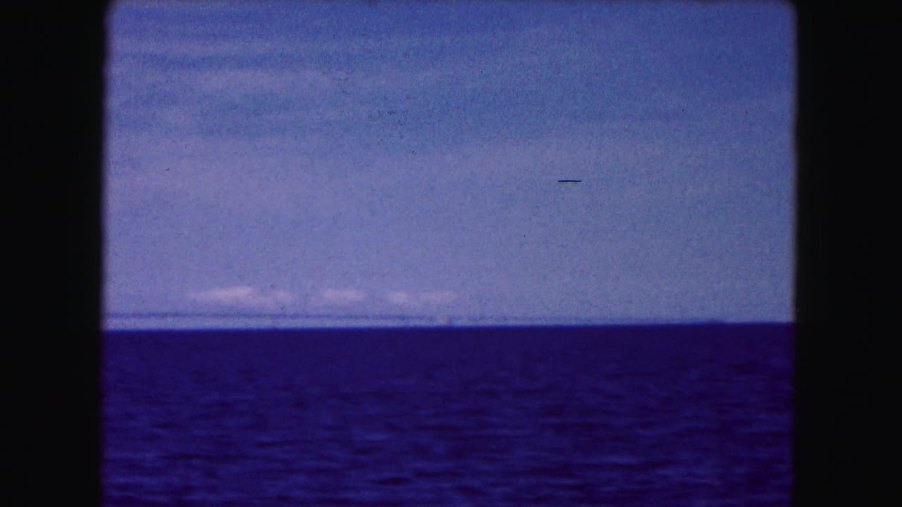 Open water below a blue sky with distant low shoreline on the horizon.