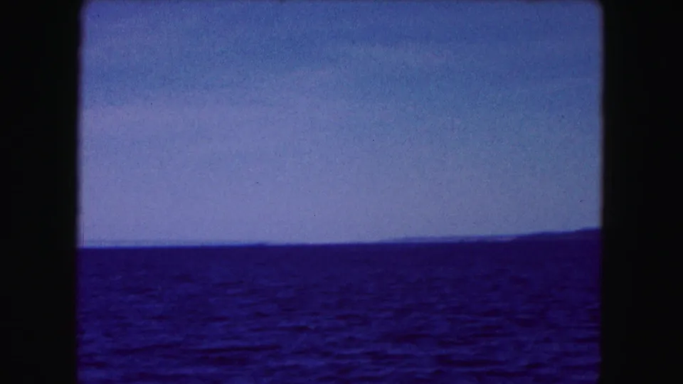 1961 8mm shoreline view near Buffalo, with blue water in the foreground and low land in the distance.