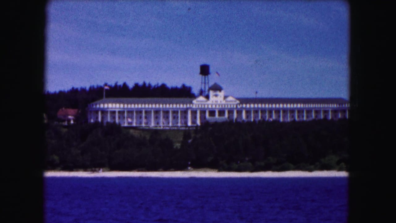 1961 8mm view of a long white lakeside building in Buffalo, New York, seen across blue water with trees and a sandy shore.
