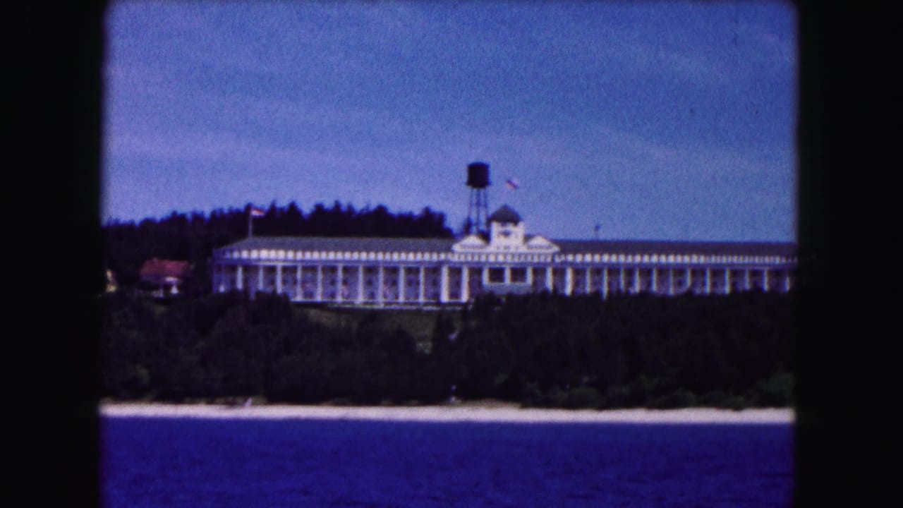White waterfront building with water tower, tree line, sandy shore, and blue lake in foreground.