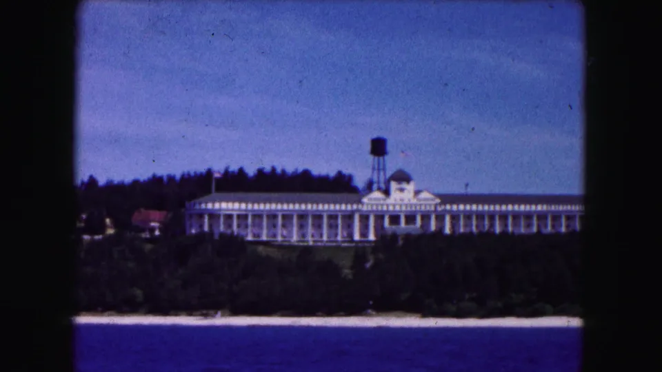 1961 8mm frame from Buffalo showing the white lakeside structure, cupola, and water tower through a dark film gate border.