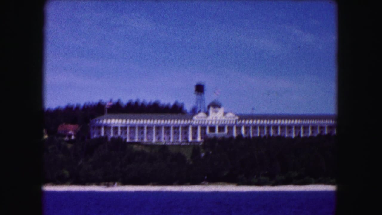 White lakeside hotel with water tower seen across trees and shoreline.