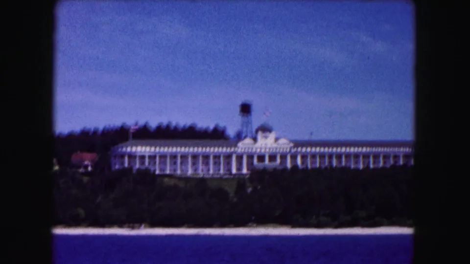 1961 Buffalo-area 8mm view of a long white lakeside resort hotel with a water tower above a wooded shoreline.
