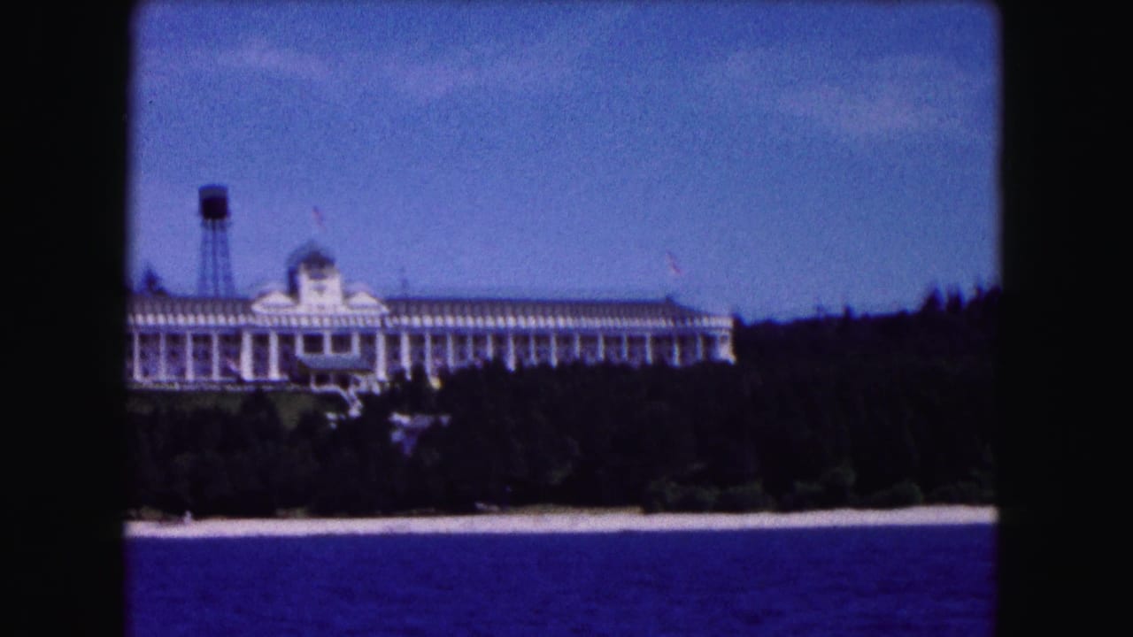 1961 Buffalo-area 8mm frame showing a large white columned building on a wooded shoreline above blue water, with a water tower nearby.