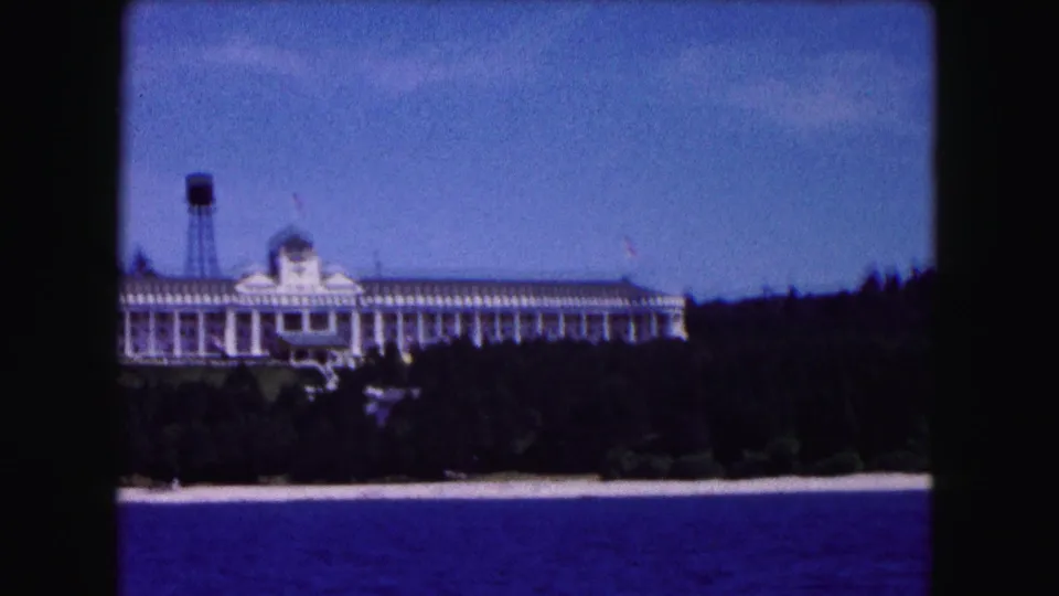 1961 Buffalo-area 8mm frame showing a large white columned building on a wooded shoreline above blue water, with a water tower nearby.