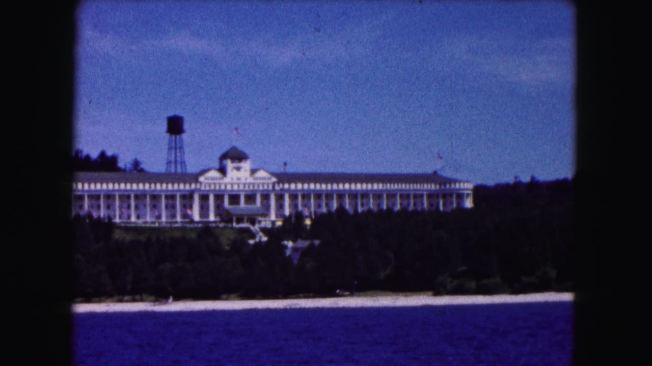 White columned building on wooded shoreline with blue water and water tower.