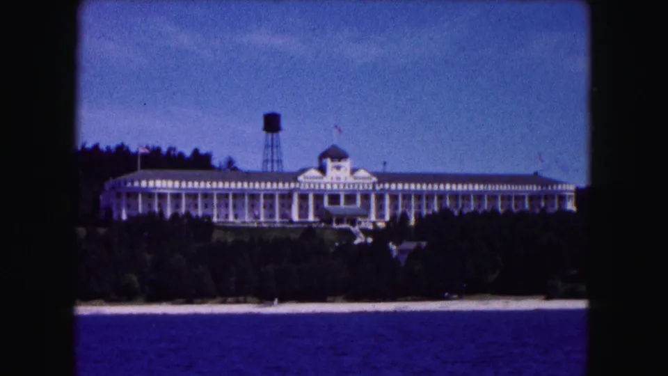 1961 Buffalo-area 8mm view of the columned white building above a wooded shoreline, with deep blue water in the foreground.