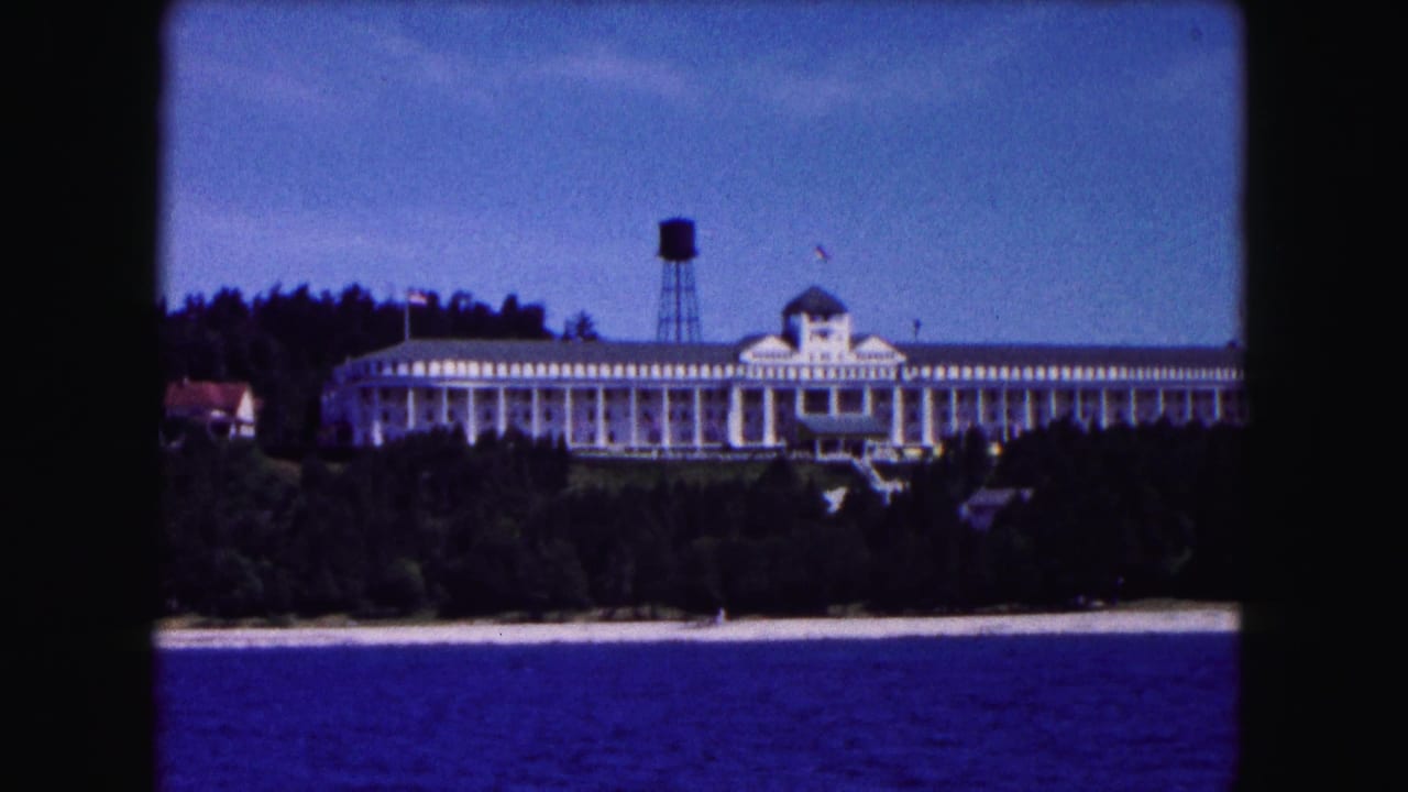 1961 Buffalo-area 8mm frame showing a large shoreline resort hotel, water tower, trees, beach edge, and blue water.