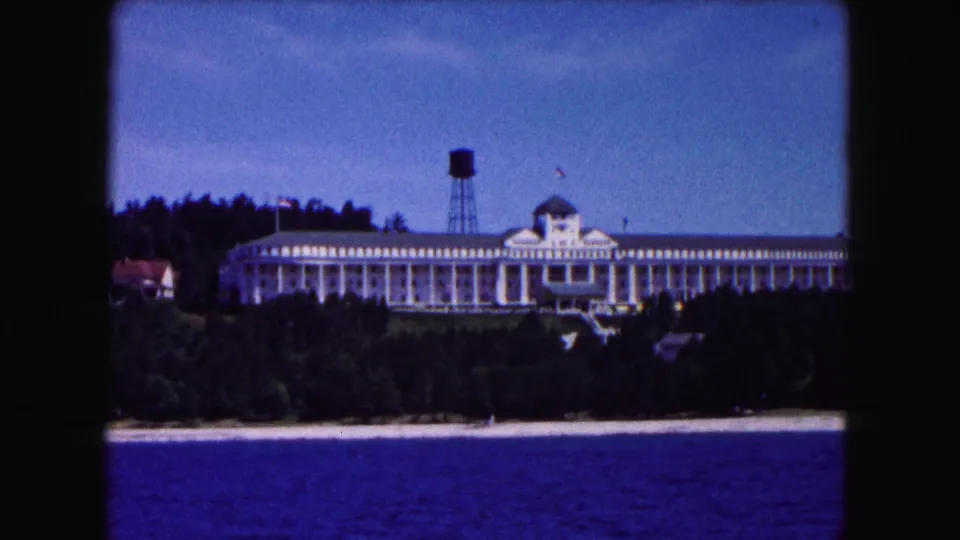 1961 Buffalo-area 8mm frame showing a large shoreline resort hotel, water tower, trees, beach edge, and blue water.