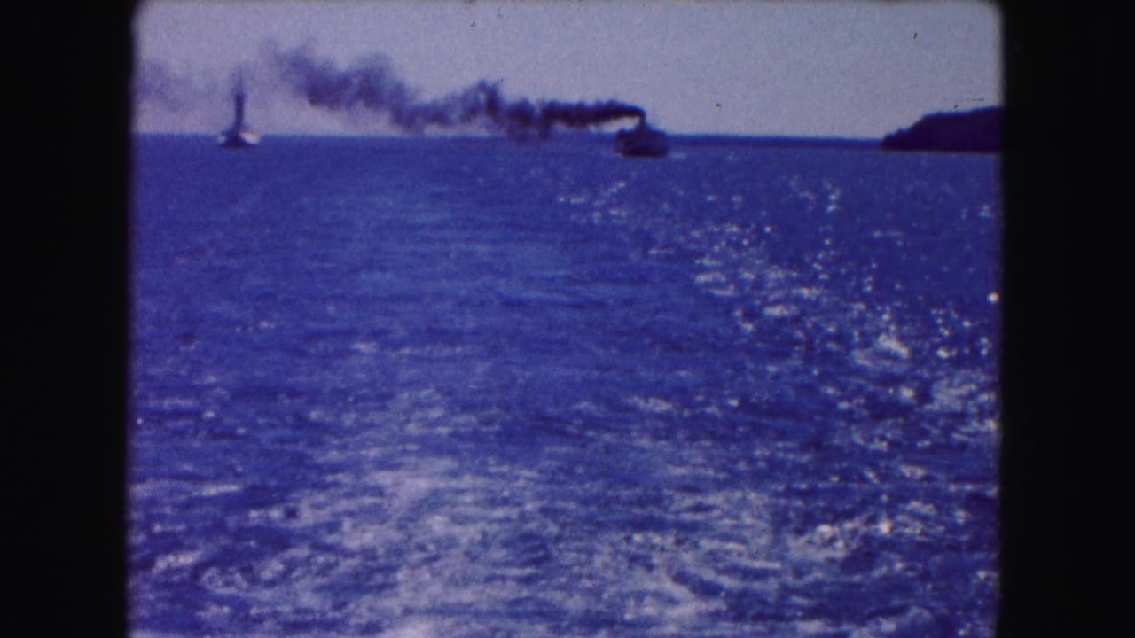 Open water seen from a moving boat with distant smoking vessels near the horizon.