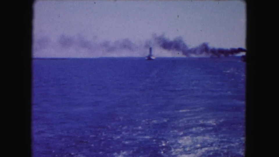 1961 Buffalo-area 8mm frame showing open water, a distant smoke plume, and small vessel silhouettes near the horizon.