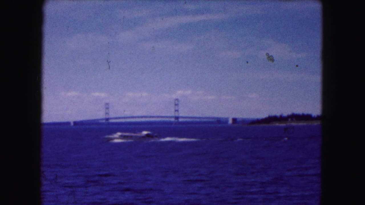 1961 8mm frame of a motorboat crossing a wide waterway near Buffalo with a suspension bridge in the background.