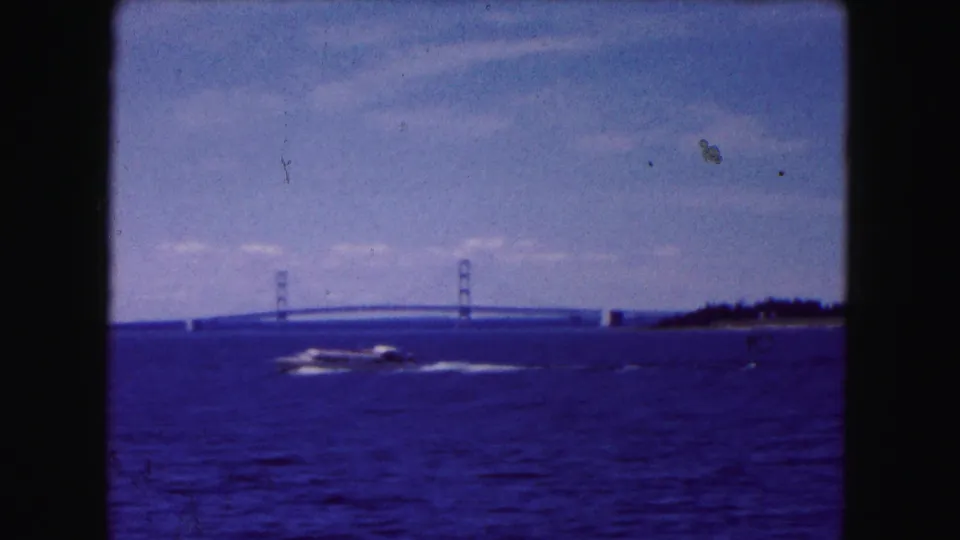 1961 8mm frame of a motorboat crossing a wide waterway near Buffalo with a suspension bridge in the background.