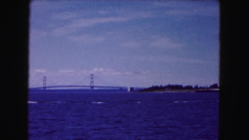 1961 8mm view near Buffalo with open water, fading boat wake, wooded shoreline, and a distant suspension bridge.