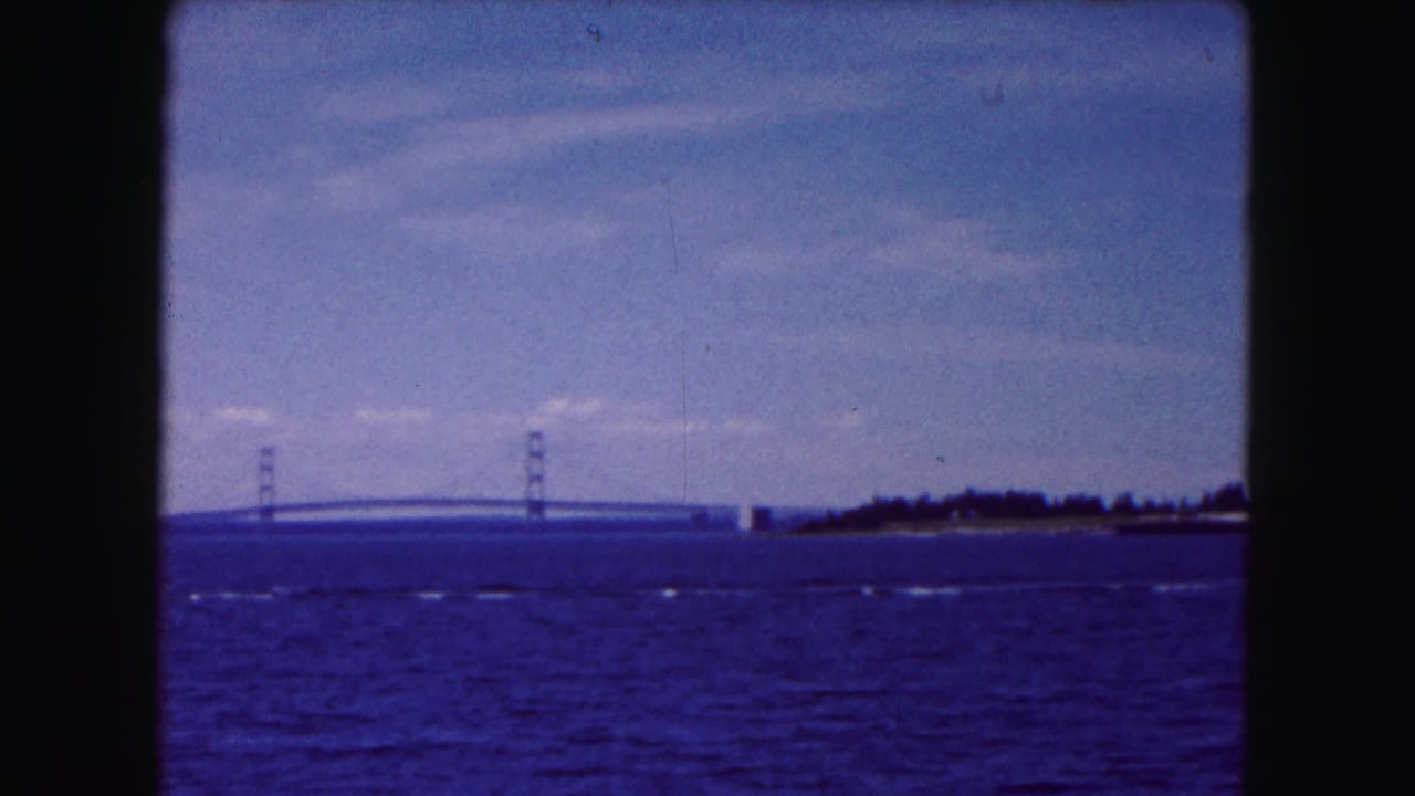 1961 home-movie view near Buffalo showing a distant suspension bridge across rippling water beneath a pale blue sky.