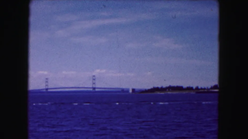 1961 home-movie view near Buffalo showing a distant suspension bridge across rippling water beneath a pale blue sky.