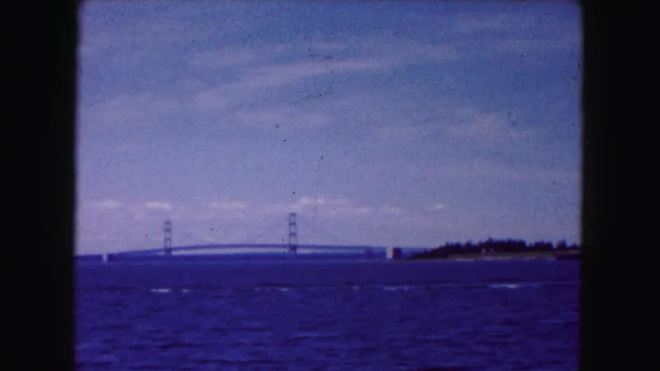 Distant bridge towers and span appear across open water, with shoreline trees at right in the 1961 Buffalo-area footage.