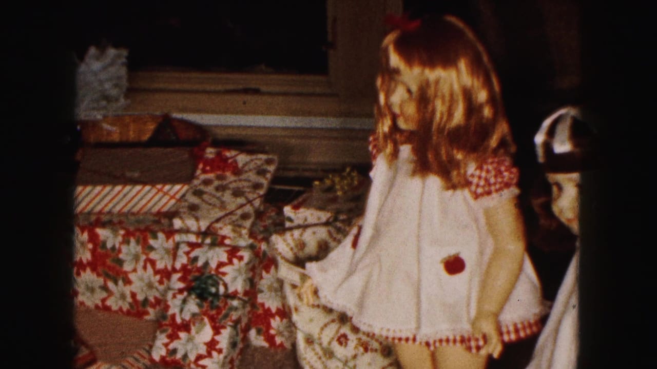 Brown-haired doll in a white dress beside wrapped Christmas presents.