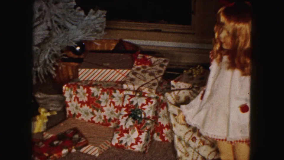 1961 Buffalo holiday interior with wrapped gifts on the carpet and the edge of a dressed doll beside them.