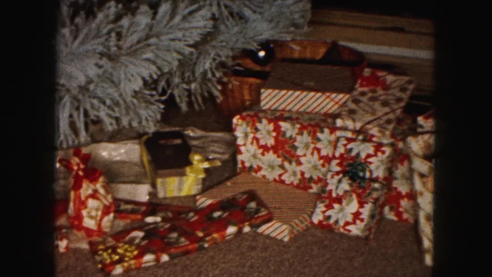 1961 Buffalo home-movie frame showing wrapped Christmas presents arranged near a small artificial tree indoors.