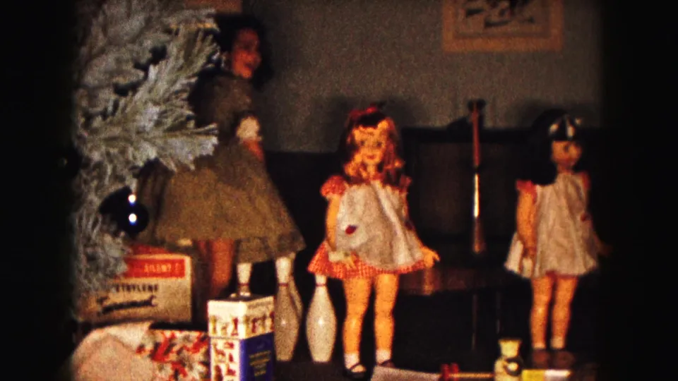 1961 Buffalo home-movie frame with a child near a Christmas tree and a display of dolls, gifts, and toy bowling pins.